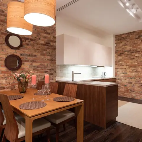 Open dining nook beside a kitchenette, exposed brick accent wall, drum pendant lights over a wood dining table set with candles and flowers