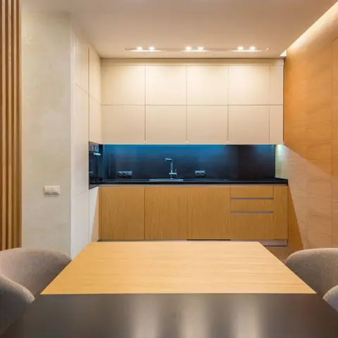 Open dining nook facing a handleless wood-and-cream kitchen with a black glass backsplash, beside a fluted wood partition wall
