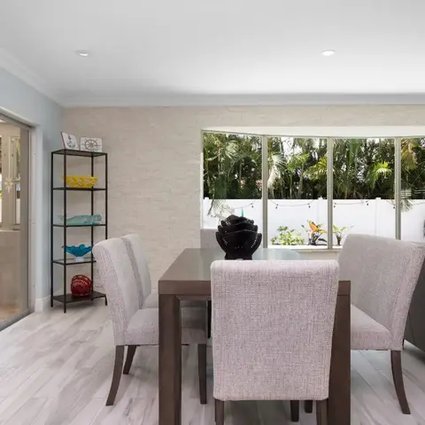 Open dining nook with a stacked-stone accent wall, dark wood table and floor-to-ceiling sliding glass doors opening onto a palm-lined patio.