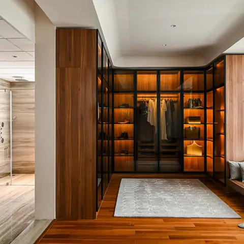 Open ensuite layout with a marble-tiled walk-in shower and freestanding tub opening onto a walnut walk-in wardrobe with backlit glass-front shelving.