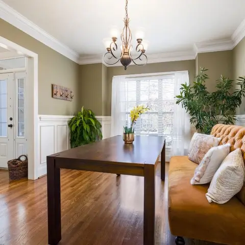 Open entry room with a mustard tufted chesterfield sofa beside a dark wood table, wainscoted walls and the front door with sidelight glass visible beyond