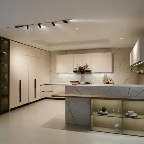 Open kitchen built around a marble waterfall island whose back face opens into lit display shelving, faced by cream matte handleless tall units