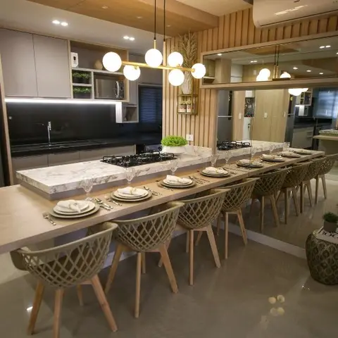 Open kitchen-dining island with a marble-look waterfall counter and built-in cooktop, a long dining table with woven rattan-back chairs