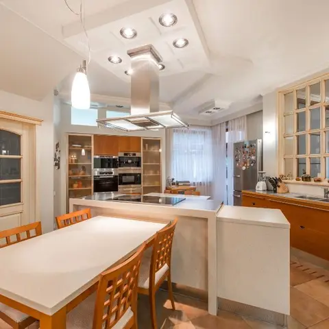 Open kitchen-dining space with a wood-cabinet island, stainless chimney hood, and a mullioned window over the sink.