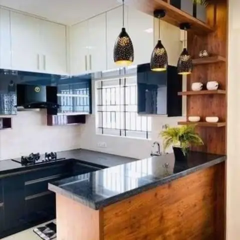 Open kitchen with a black granite breakfast counter on a wood base, three star-cutout pendant lights, and a wooden overhead display shelf with trailing plants.