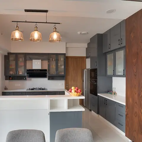 Open kitchen with a glossy grey island breakfast counter under three amber glass pendant lights, a built-in oven and microwave column