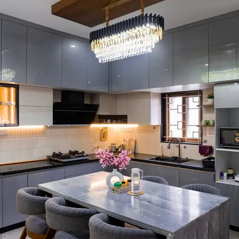 Open kitchen with glossy grey cabinetry, a black stone island doubling as a marble-topped dining table with velvet tub chairs, a glass-front crockery display
