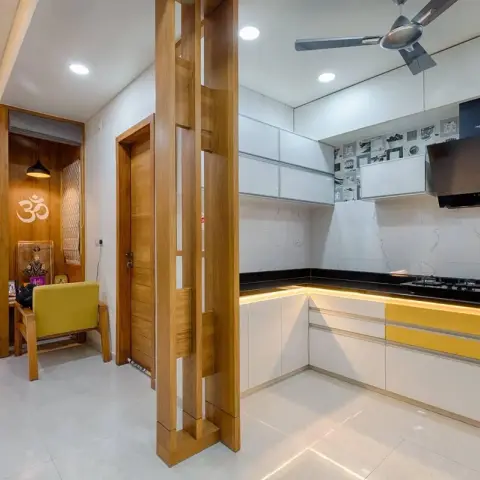 Open kitchen with mustard-yellow accent shutters and a black granite counter, opening onto a wood-panelled pooja nook with an Om wall motif.