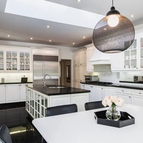 Open kitchen with white shaker cabinetry, a black granite island with glass-front lower panels, a large mesh-globe pendant light