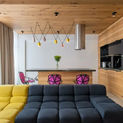 Open living and kitchen space with a two-tone yellow and navy modular sofa, magenta faceted bar stools at the wood island