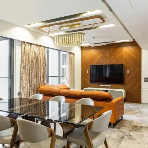 Open living-dining in a high-rise flat: a chevron walnut TV wall facing a tan quilted-leather sofa, a black marble dining table for eight in the foreground