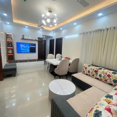 Open living-dining room with a cove-lit tray ceiling, a marble-backed TV unit with lit display niches, a round marble coffee table
