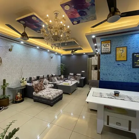 Open living-dining space with a crystal chandelier, printed ceiling panels, a floral upholstered sofa
