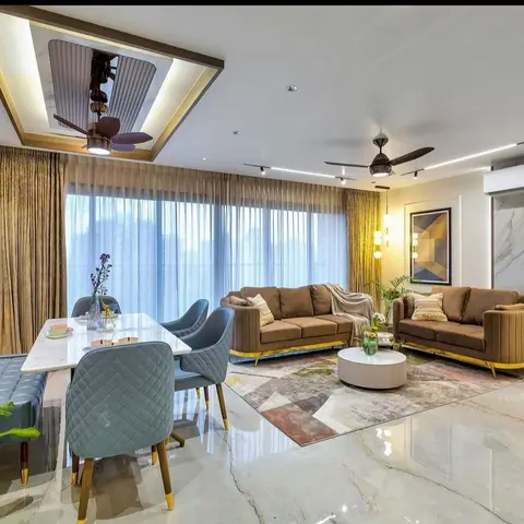 Open living-dining space with a channel-tufted brown sofa set on a patchwork rug, a marble-clad accent wall and a marble-top dining table with teal quilted