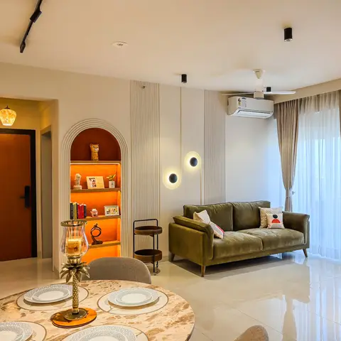 Open living-dining space with a round marble-top dining table set for four, an olive velvet sofa against fluted wall panelling