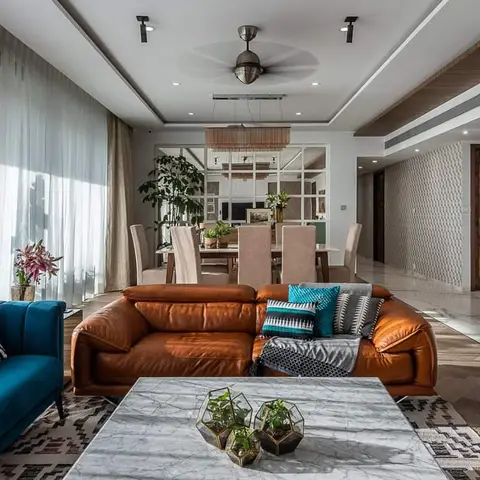 Open living-dining space with a cognac leather sofa and teal velvet loveseat around a marble coffee table styled with glass terrariums