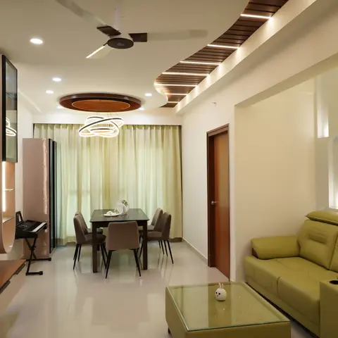 Open living-dining space with an olive leather sofa beside a backlit arched wall panel, a round dining table lit by a ring pendant chandelier