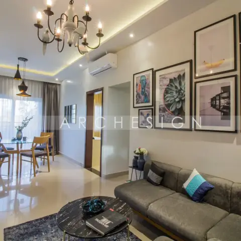 Open living-dining where an olive-grey L-sofa sits under a nine-frame gallery wall of photo prints, a black marble round table on a blue rug in front of it