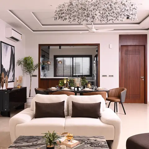 Open living-dining with a sprawling crystal-twig chandelier over a laid black marble dining table, curved cream sofas in front