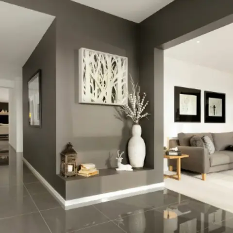 Open living room with a fireplace and grey sofa, seen past a styled entrance hallway with a charcoal accent wall niche and console vignette.
