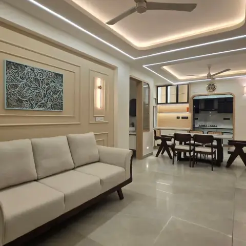 Open living room with a teak-framed cream three-seater against a wall of slim mouldings and a teal carved-motif canvas