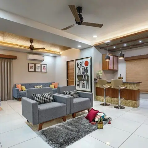 Open living room with grey fabric sofas and armchairs around a grey shag rug, a framed pop-art print, and a home bar corner with wood-and-stone counter