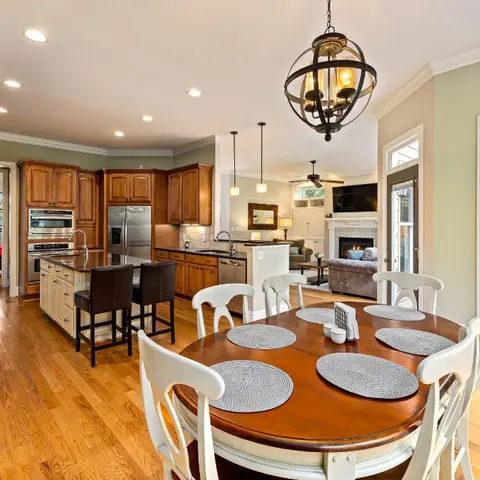 Open-plan American home showing a wood-cabinet kitchen island, round dining table and a living room with fireplace beyond, seen together in one frame.