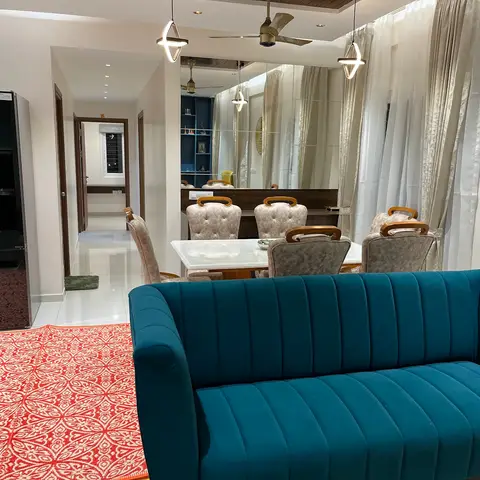 Open-plan apartment corner showing the kitchen, a tufted-chair dining set reflected in a large mirror, and a teal channel-tufted sofa together in one frame.