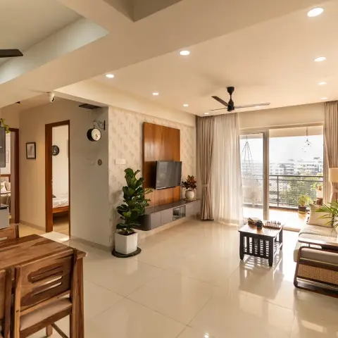 Open-plan apartment interior combining a wood dining table with woven basket, a living area with a wood-toned TV wall and beige sofa