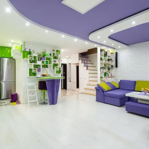 Open-plan apartment with a bright green high-gloss kitchen beside a purple-upholstered living zone and a staircase, all visible in one frame