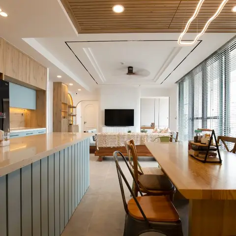 Open-plan apartment with a light-blue fluted kitchen island, wood dining table, and a TV lounge visible beyond