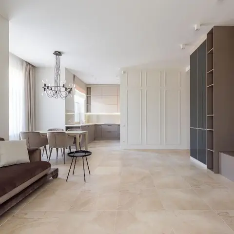 Open-plan apartment with a plum velvet sofa in the foreground, dining table and kitchenette beyond, panelled wall and a bubble-drop chandelier