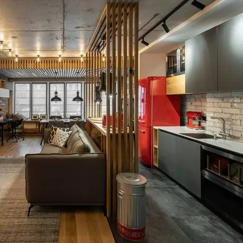 Open-plan apartment with a wood-slat partition separating a grey industrial-style kitchen with a red retro fridge from the living and dining zones