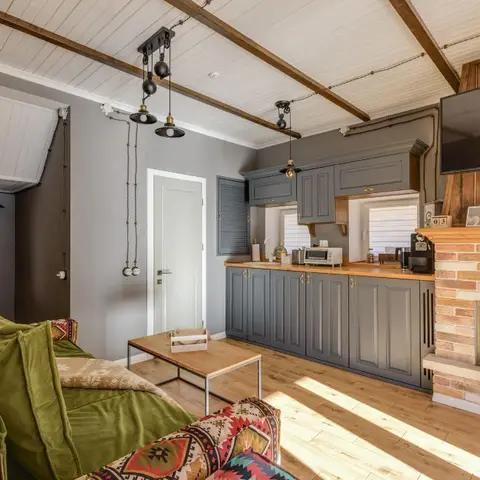 Open-plan cabin living-kitchen with a brick fireplace and wall-mounted TV, grey shaker kitchen cabinetry with a wood countertop