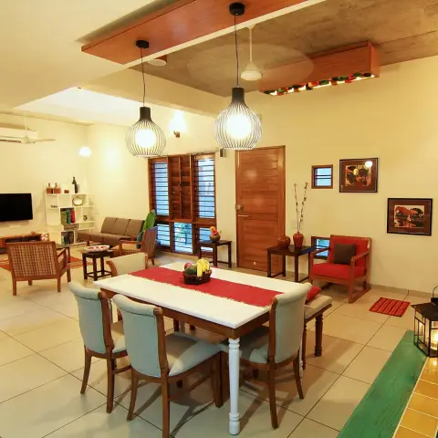 Open-plan dining and living area with a marble-topped wood dining table under cage pendant lights, a wood-slat door and window