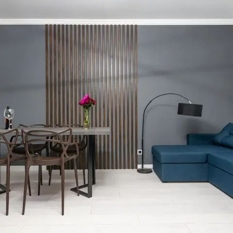Open-plan dining and living area with a wood slat accent wall divider, a dark wood dining set, and a navy corner sofa.