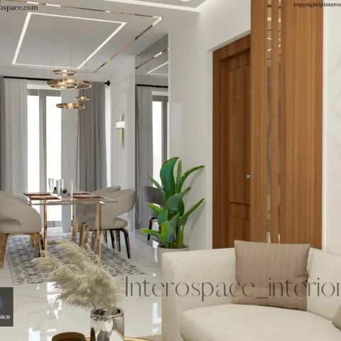 Open-plan dining and living area with a marble-top dining table under a cluster of gold ring pendants, opening onto a cream sofa beside a fluted wood door frame