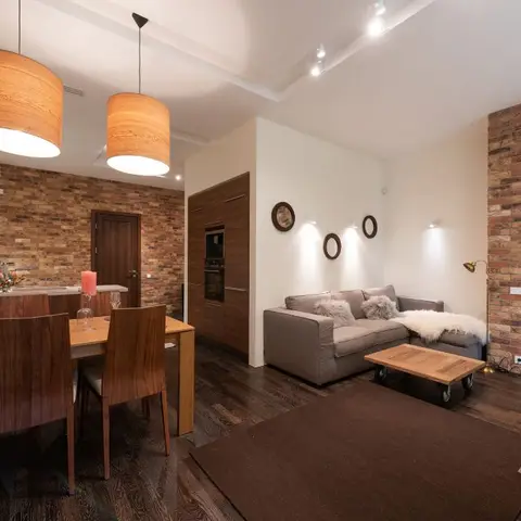 Open-plan dining and living area with an exposed brick accent wall, a walnut dining set, and twin wood-drum pendant lights over the table.