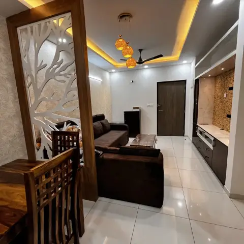 Open-plan dining and living area divided by a tree-branch cutout wood partition, with amber cluster pendant lights, a brown sofa, and a stone-clad TV wall.
