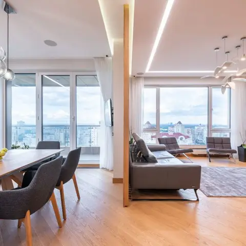 Open-plan dining and living area divided by a wood post, with bubble pendant lights over the table and a sculptural chandelier over grey lounge seating against