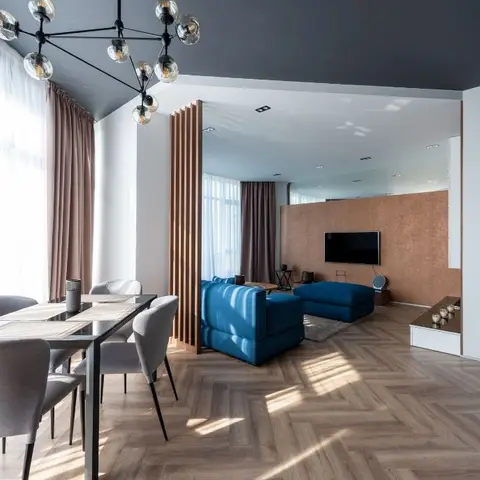 Open-plan dining and living area with a molecular chandelier over a grey dining set, a wood-slat partition