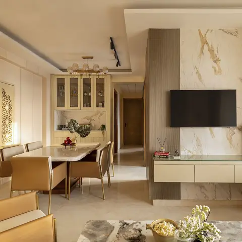 Open-plan dining and living area with a backlit jaali wall panel beside the dining table and a book-matched marble TV feature wall opposite.