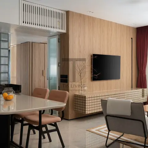 Open-plan dining and living area with a glass-block partition, wood-panelled TV wall over a quilted wood console, and maroon curtains by the window.