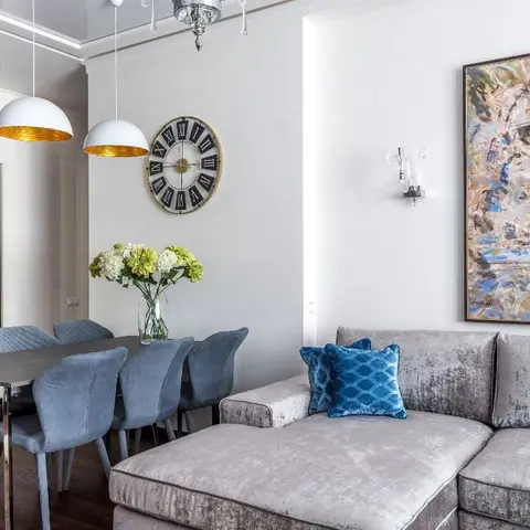 Open-plan dining and living space with slate-blue velvet dining chairs under gold-lined dome pendants