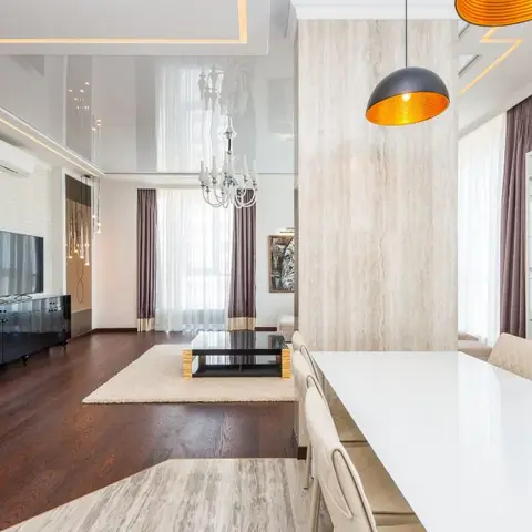 Open-plan dining and living space with a white marble dining table, a black-and-orange dome pendant, a travertine-clad column