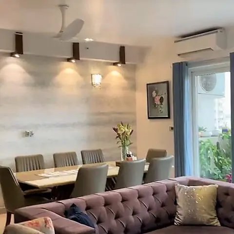 Open-plan dining and living space with a six-seat dining table against a textured stone-clad accent wall lit by brass picture lights