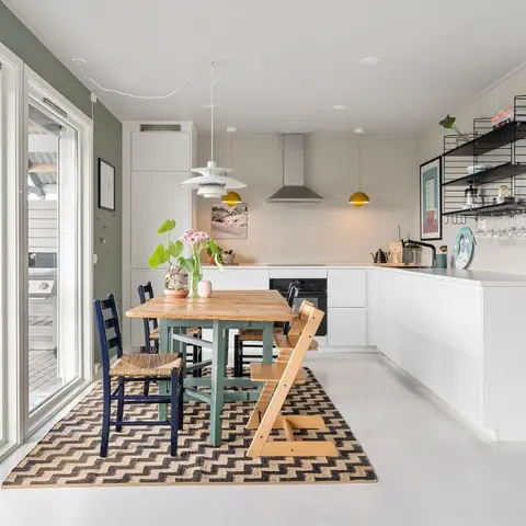 Open-plan dining area with a wood table and mismatched chairs including a wooden high chair, on a chevron-pattern rug