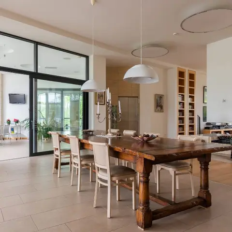 Open-plan dining area with a heavy rustic wood table and white chairs, adjoining a living room with a built-in bookshelf and fireplace nook beyond.