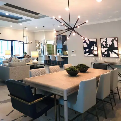 Open-plan dining, living and kitchen area under a sculptural branch-style chandelier with a triptych of tree-branch wall art behind the dining table.