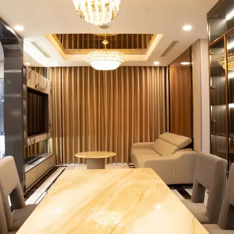 Open-plan dining-living space with a marble dining table in the foreground, a gold-curtained living zone with sofa and marble-clad TV wall behind